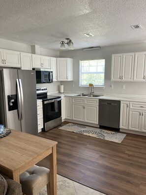 Een moderne keuken met witte kasten, roestvrijstalen apparatuur, een houten eettafel en een vloerkleed met een patroon.