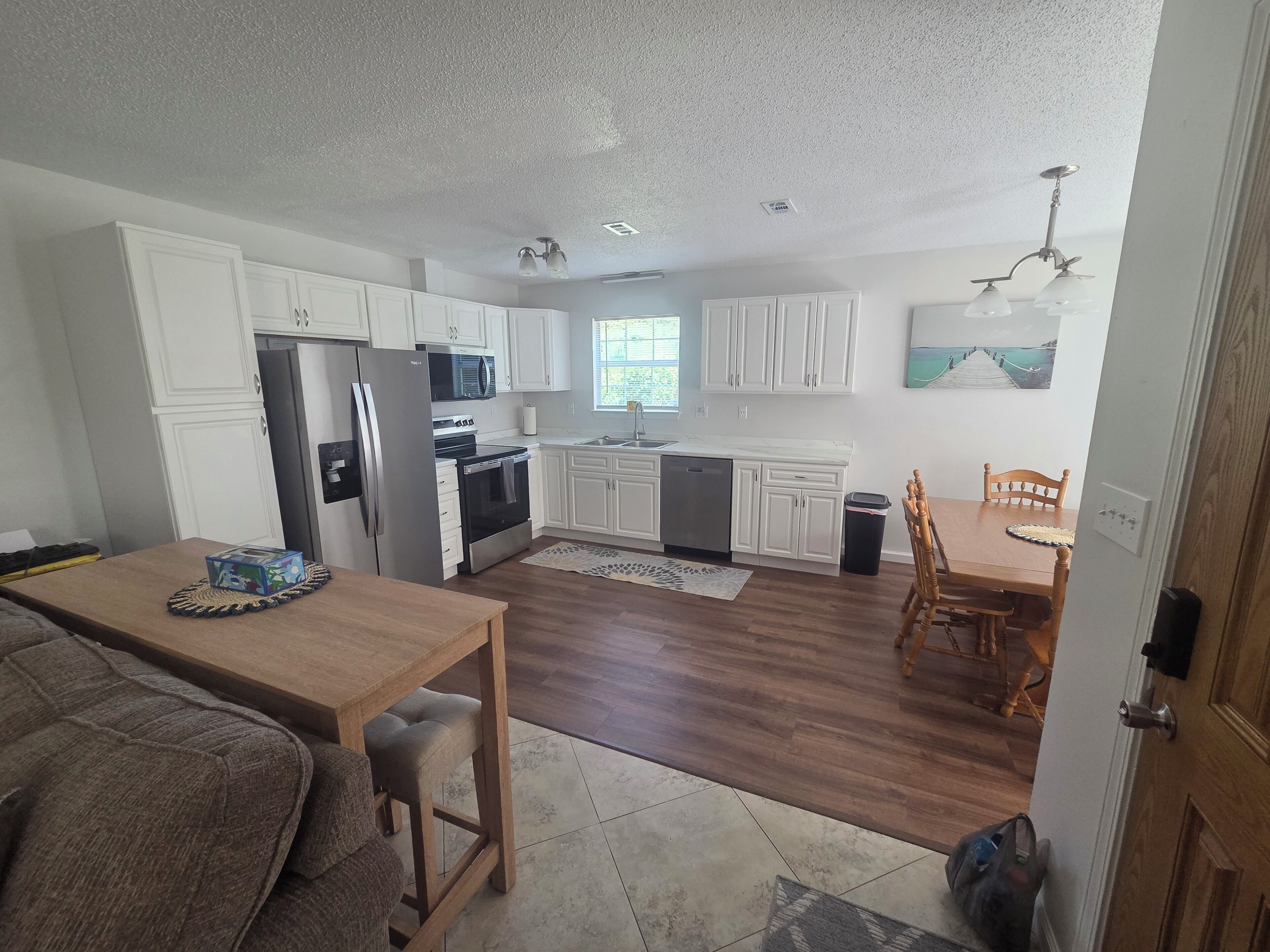 A modern kitchen with white cabinets, stainless steel appliances, and a dining area with a wooden table and chairs.