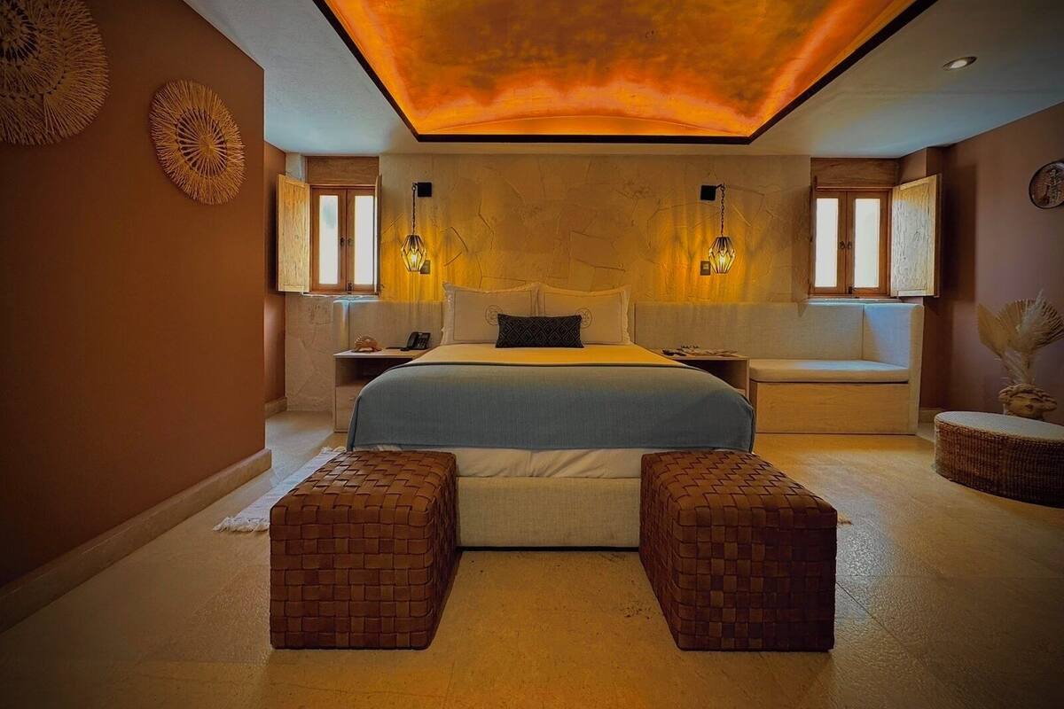 A bedroom with a large bed, two nightstands, a bench, and a ceiling light fixture.