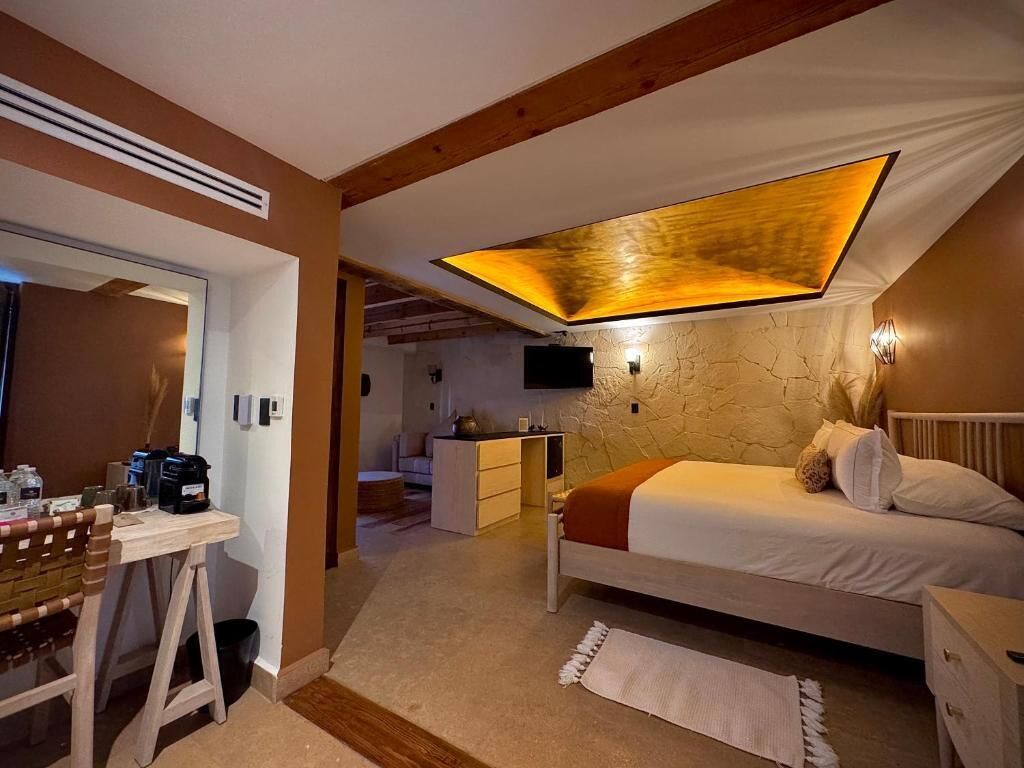 A bedroom with a bed, bedside table, and a desk with a chair. There is a ceiling light fixture and a wall-mounted TV.