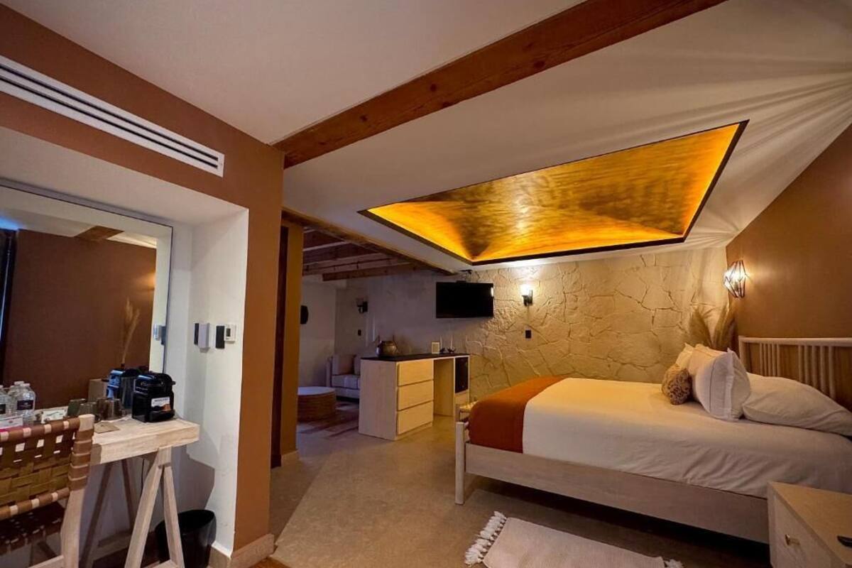 A bedroom with a bed, bedside table, and a desk with a chair. There is a ceiling light fixture and a wall-mounted TV.