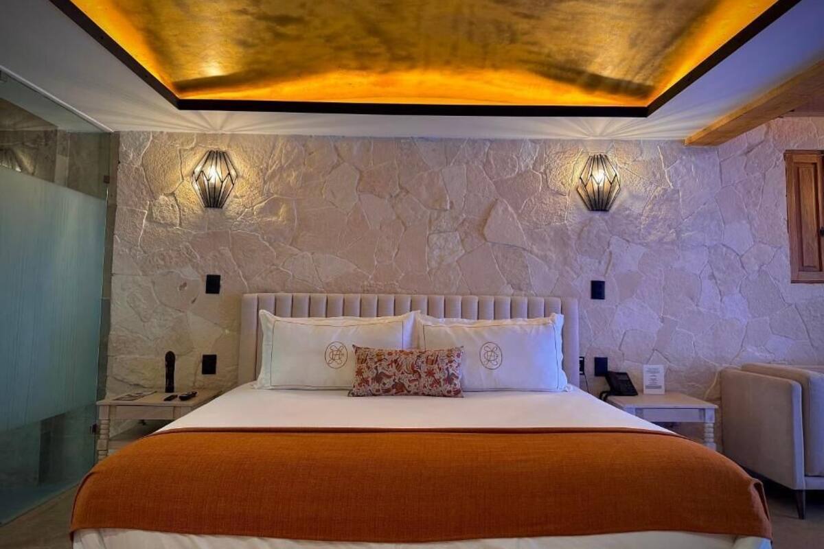 A bedroom with a stone wall, a bed with white bedding, two wall-mounted lights, and a wooden headboard.