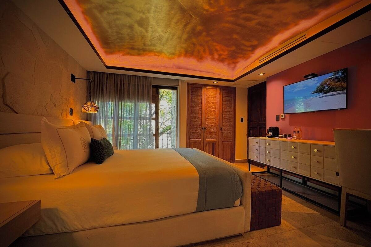A bedroom with a bed, a dresser, a TV, and a ceiling with a light design.