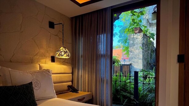 A bedroom with a bed, a bedside table, a lamp, and a view of a garden through a sliding door. - Casa Laja - Hotel Boutique (San Miguel de Allende)