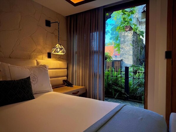 A bedroom with a bed, a bedside table, a lamp, and a view of a garden through a sliding door. - Casa Laja - Hotel Boutique (San Miguel de Allende)