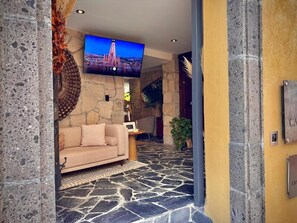 A stone-floored lobby with a sofa and a flat-screen TV mounted on the wall. - Casa Laja - Hotel Boutique (San Miguel de Allende)