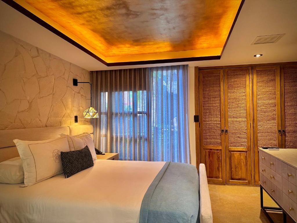 A bedroom with a bed, bedside lamp, curtains, a wardrobe, and a vanity.