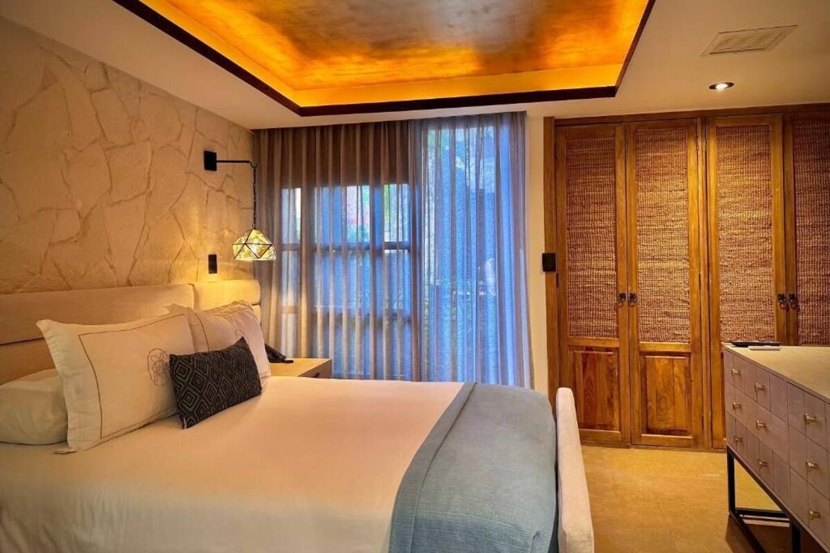 A bedroom with a bed, bedside lamp, curtains, a wardrobe, and a vanity.