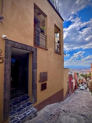 A narrow cobblestone street with a building featuring a stone staircase leading to an entrance. - Casa Laja - Hotel Boutique (San Miguel de Allende)