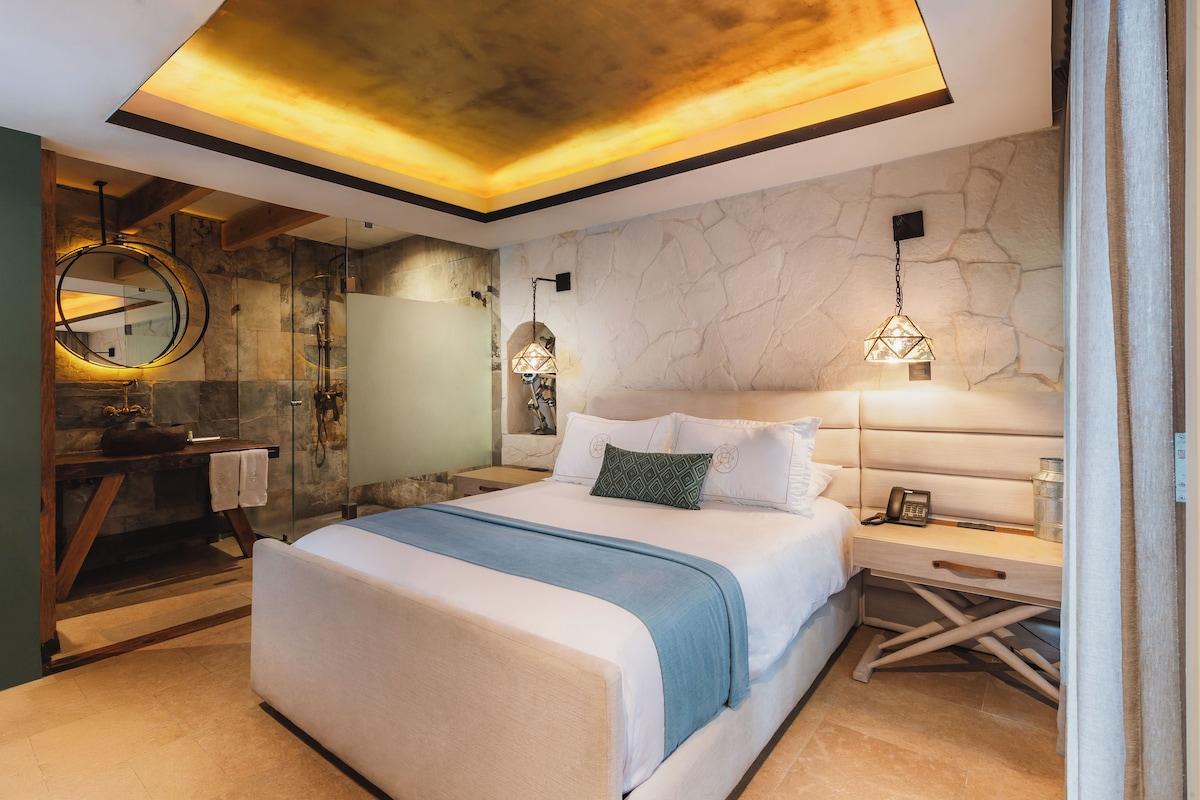 Quarto moderno com cama grande, box de vidro e parede de pedra.