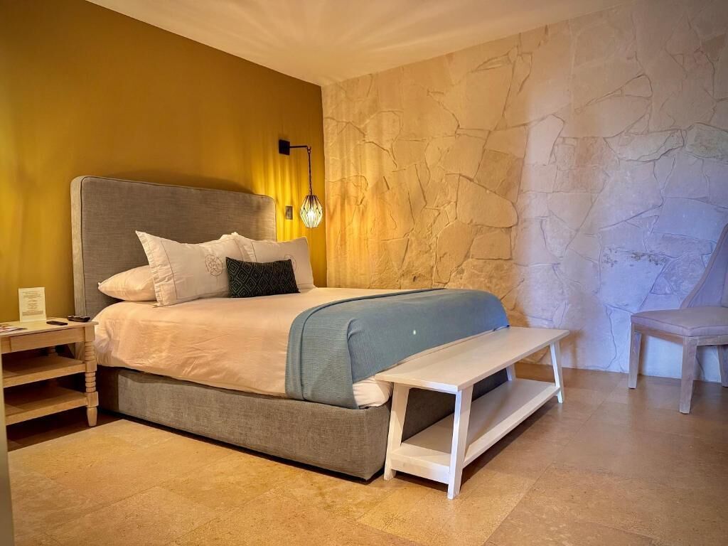 A bed with a headboard, bedside tables, a bench, and a stone wall.