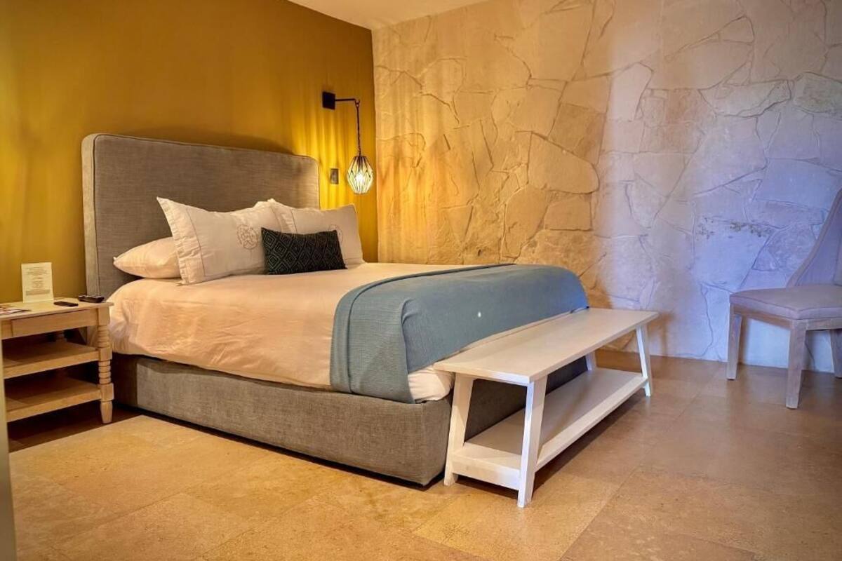 A bed with a headboard, bedside tables, a bench, and a stone wall.