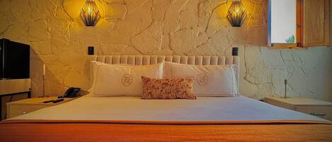 A bedroom with a stone wall, a bed with white bedding, two wall-mounted lamps, and a window with a view.