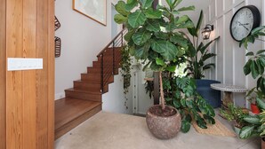 Eine Treppe mit Holzdielen, ein Blumentopf, eine Wanduhr und ein kleiner Tisch mit gemusterten Abdeckungen.