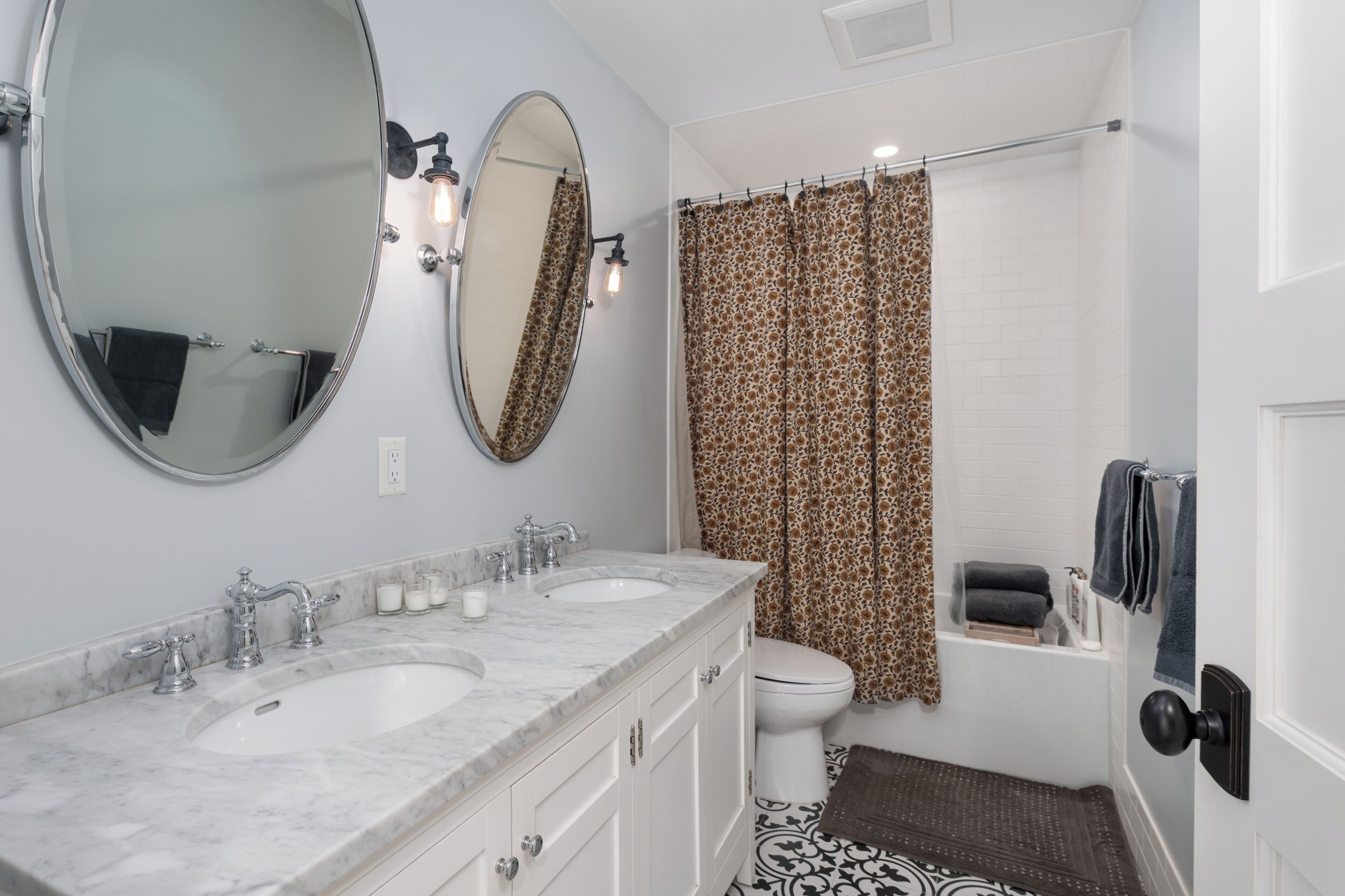 Une salle de bain avec deux lavabos, des toilettes, une douche avec un rideau à motifs et un miroir.