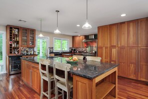 A kitchen with wooden cabinets, a granite countertop, and a central island with bar stools. - Sauna Barn Wellness Retreat on 2 Acres (Princeton)