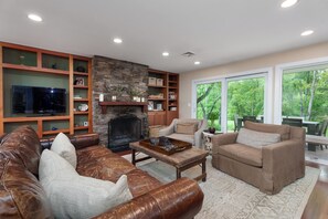 A living room with a fireplace, leather sofas, a coffee table, and a bookshelf. - Sauna Barn Wellness Retreat on 2 Acres (Princeton)