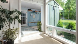 Ein Flur mit einem großen Fenster, einem Blumentopf, einer Bank und einer Wand mit Körben und Taschen.