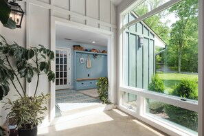 A hallway with a large window, a potted plant, a bench, and a wall with baskets and bags. - Sauna Barn Wellness Retreat on 2 Acres (Princeton)