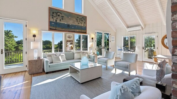 A spacious living room with a high ceiling, large windows, and a painting above the sofa.