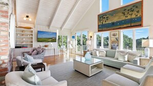 A spacious living area with a high ceiling, a large TV, and a painting.
