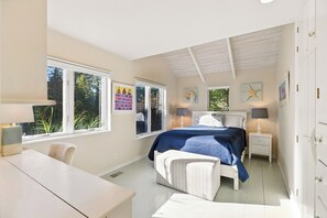 A bedroom with a bed, bedside tables, a desk, and large windows.