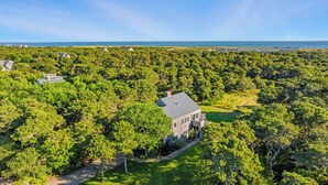 A large house surrounded by dense forest with a view of the ocean.
