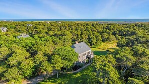 A large house surrounded by dense forest with a view of the ocean.