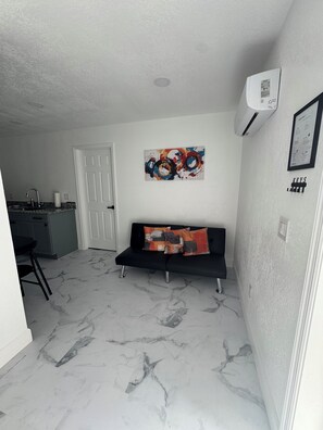 A modern living space with a black sofa, a colorful abstract painting, a white door, and a kitchen area.