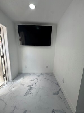 A room with a flat-screen TV mounted on the wall, marble flooring, and a door leading outside.