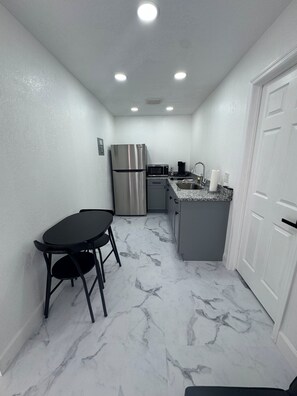 A compact kitchen with a refrigerator, microwave, sink, and a dining area with a table and chairs.