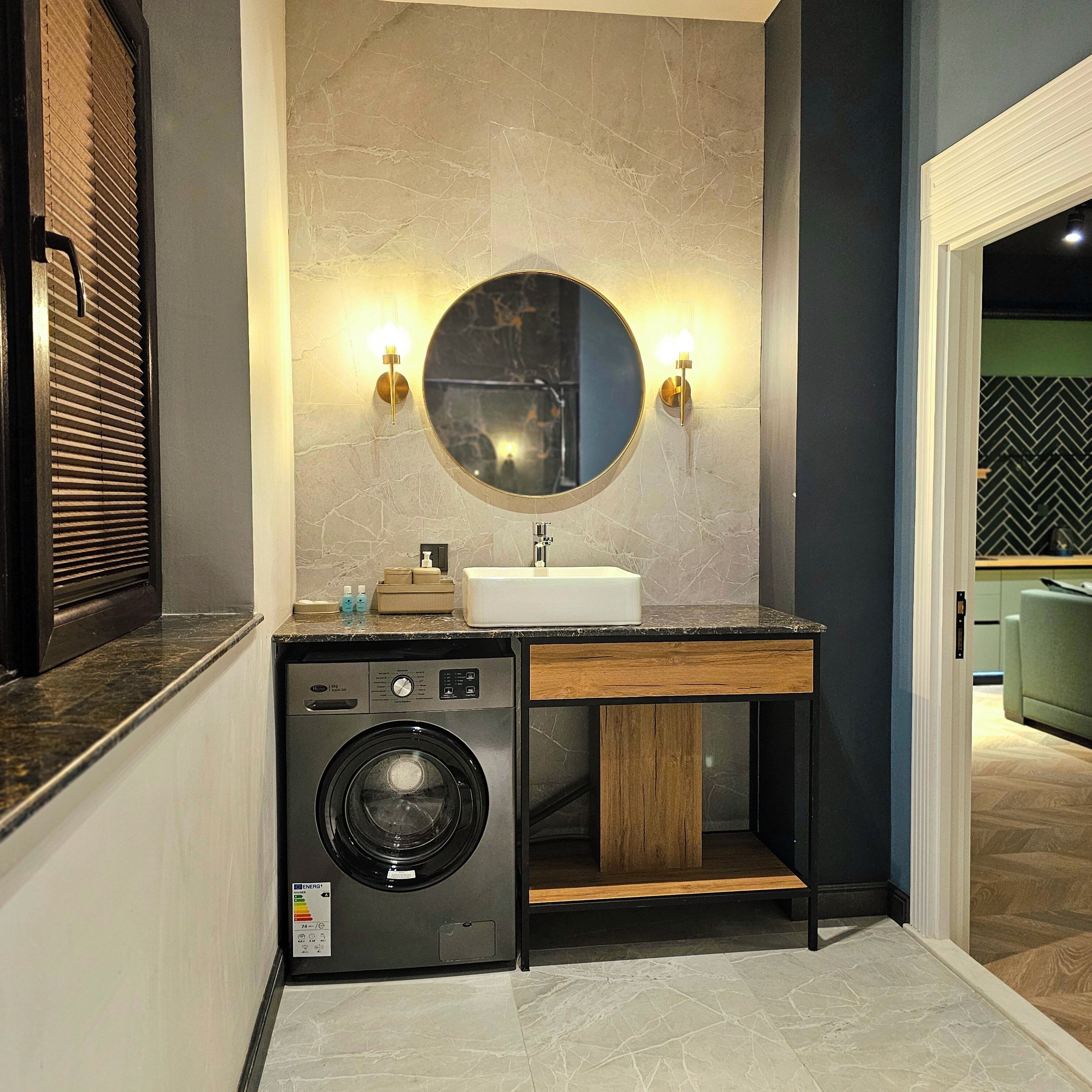Une salle de bain moderne équipée d’un lave-linge intégré, d’un lavabo et d’un miroir rond agrémenté d’appliques murales.
