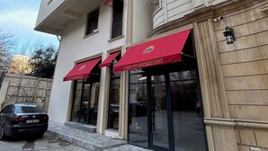 Un edificio de varios pisos con entrada a nivel de calle, grandes ventanales de vidrio y un toldo rojo con letreros.