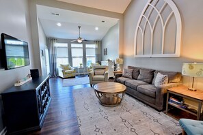 A living room with a sofa, coffee table, TV, and a large arched window.