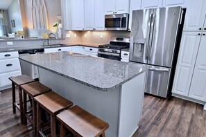 Una cocina con gabinetes blancos, encimera de granito, electrodomésticos de acero inoxidable y taburetes de madera.
