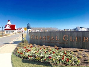 A Coastal Club sign with a speed limit sign, a lighthouse, and a flower bed.