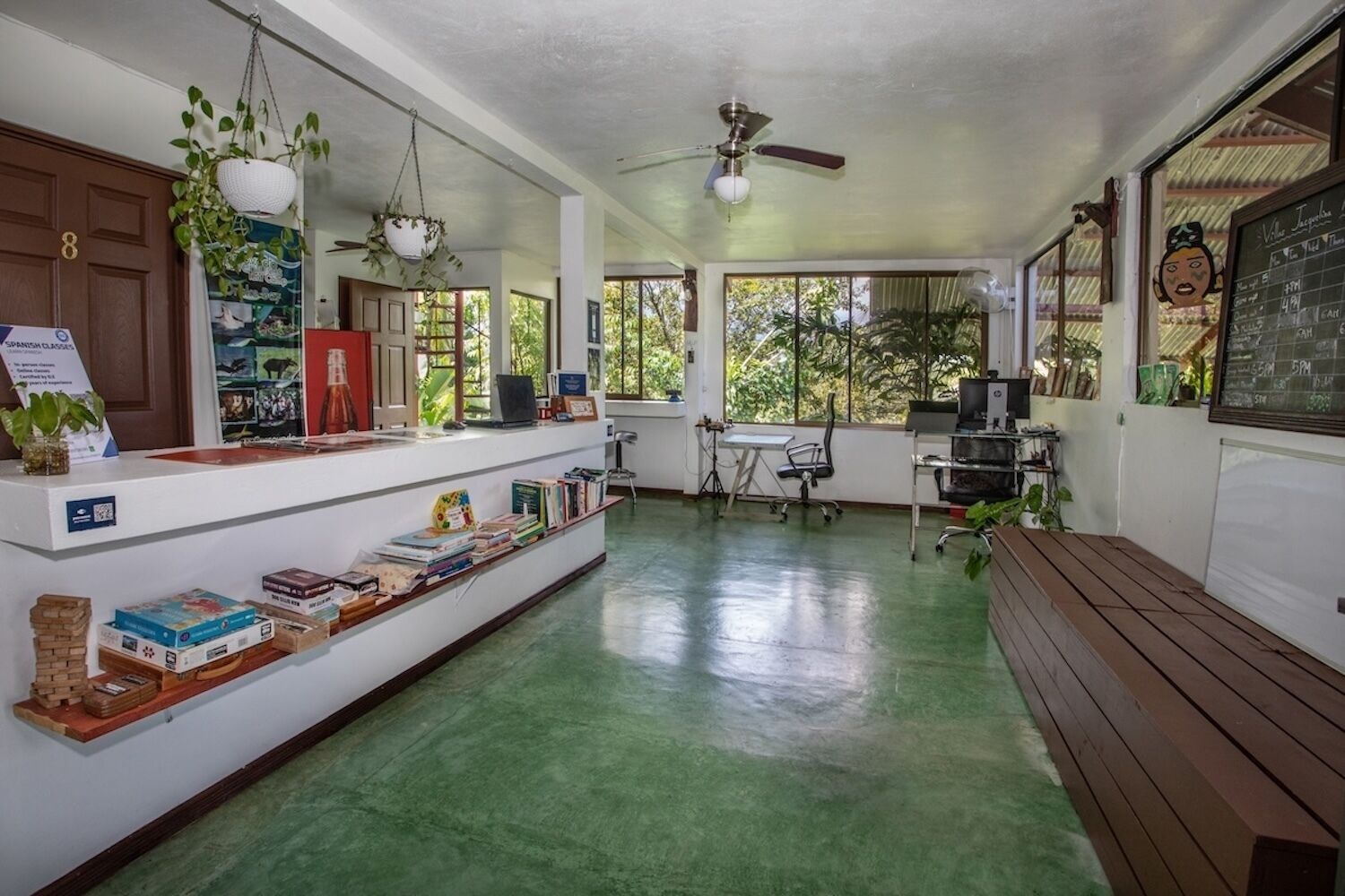 Ruime kamer met een groene vloer, een houten bank, een bureau met een computer en een krijtbordmenu.
