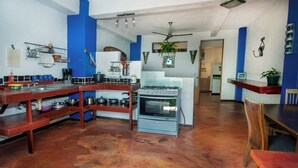 A kitchen with a gas stove, wooden shelves, and a dining area with a table and chairs. - Cozy 1-bedroom apartment with AC in tranquil Quepos (Quepos)
