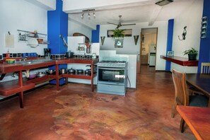 Een keuken met een gasfornuis, houten planken en een eethoek met een tafel en stoelen.