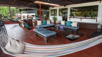 A covered outdoor seating area with a hammock, chairs, and a table.