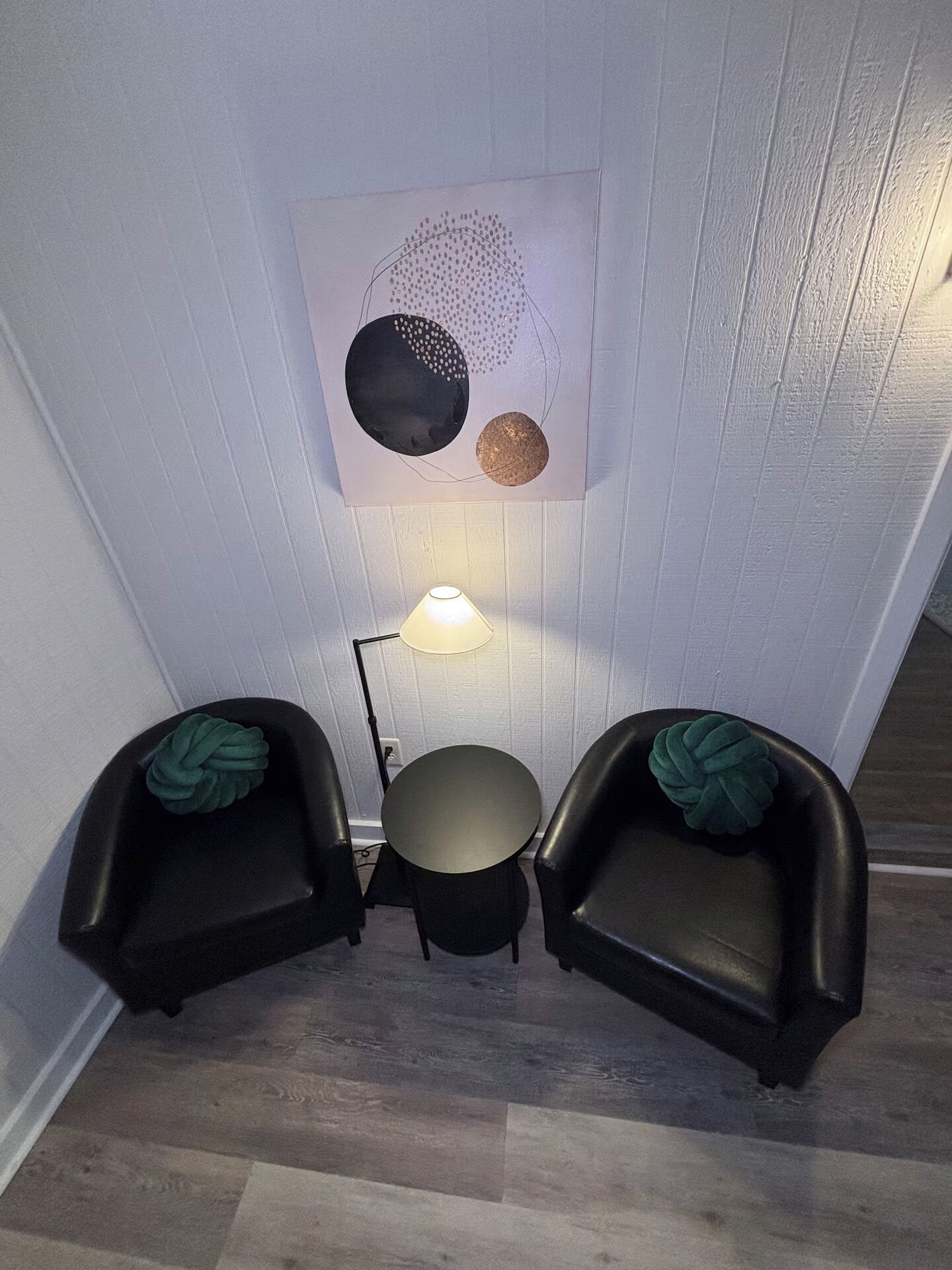 Une pièce comprenant une table ronde, deux chaises, une lampe fixée au mur et une œuvre d’art abstraite.