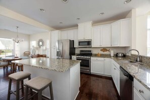 A kitchen with white cabinets, granite countertops, stainless steel appliances, and a central island with stools. - Coastal Club * 31424 * 3BR Townhouse 31424 w 2.5 B (Lewes)