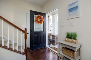 A hallway with a dark door, a staircase, a small table with plants, and a framed picture on the wall. - Coastal Club * 31424 * 3BR Townhouse 31424 w 2.5 B (Lewes)