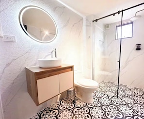 Ein Badezimmer mit Marmorwand, einem runden Spiegel, einem Waschbecken und einer Toilette.