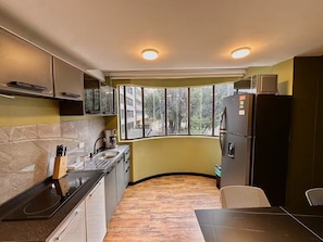 A compact kitchen with a built-in stove, a sink, and a refrigerator. There is a window providing a view of the outside. - HF Lujo moderno 3 dormitorios. Parque 93 (Bogotá)