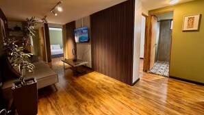 Una sala de estar moderna con suelo de madera, un sofá, un televisor y una planta.