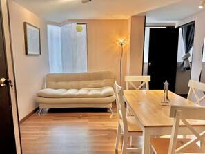 Ein Zimmer mit einer Couch, einem Esstisch mit Stühlen, einer Stehlampe und einer Tür.