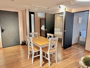 Ein modernes Hotelzimmer mit einem Holztisch, weißen Stühlen, einer kleinen Pflanze und einem Bett mit weißem Kopfteil.