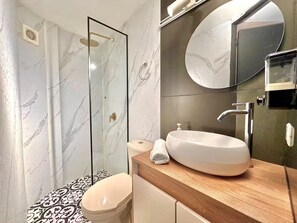 Ein Badezimmer mit Duschkabine, weißem Waschbecken, rundem Spiegel und fliesenbelagtem Boden.