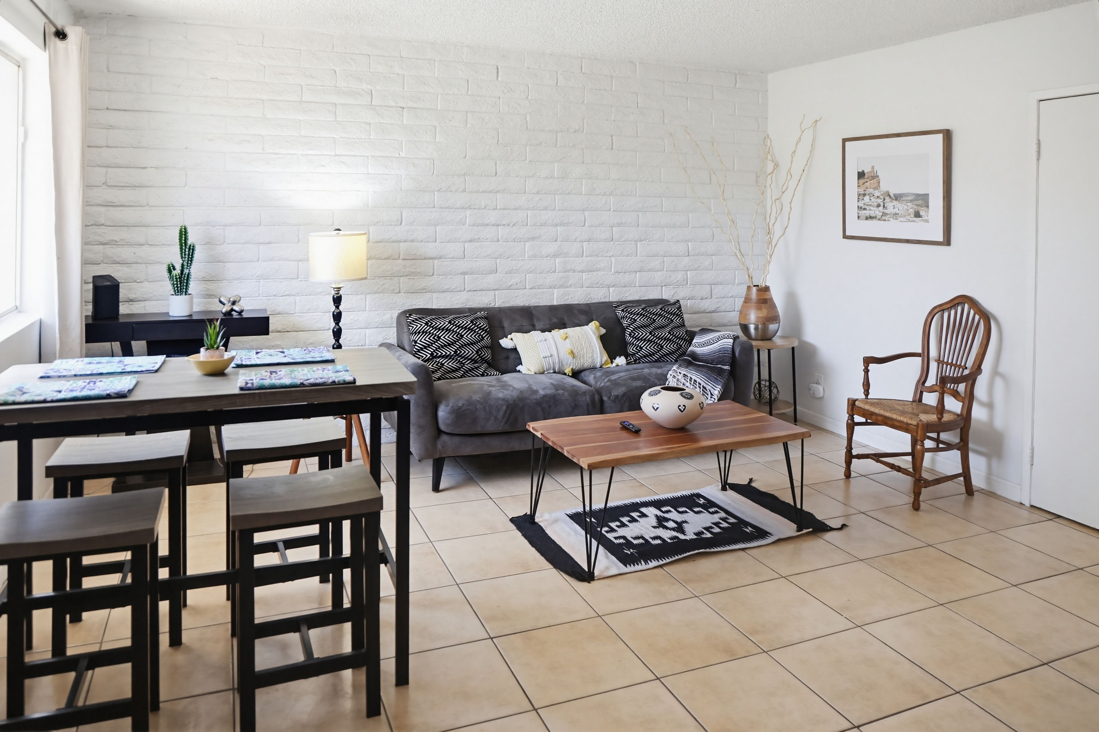 A living room with a sofa, a wooden chair, a coffee table, a dining table with chairs, a lamp, and a framed picture on the wall.